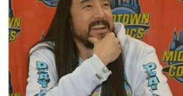 Steve Aoki smiling, wearing a colorful hoodie at a signing event, promoting "Last of My Enemies" with vibrant energy.