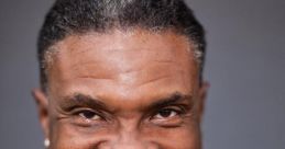 Keith David, known for his role in Spawn, smiles warmly in a stylish black and red outfit against a neutral background.