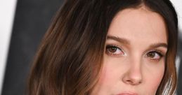 Millie Bobby Brown showcasing her glamorous look with soft waves and natural makeup at a high-profile event.