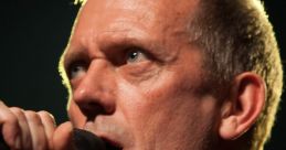 Hugh Laurie with a casual hairstyle, smiling at a public event, showcasing his distinctive style and charismatic presence.