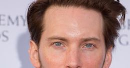 Troy Baker at a red carpet event, showcasing his stylish look with a formal suit and distinctive hairstyle.
