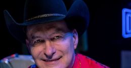 Joe Bob Briggs smiles in a vibrant red shirt with floral embellishments and a cowboy hat, highlighting his unique style.