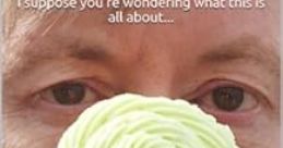 Nick Abbot holds a green cupcake adorned with dark sprinkles, pondering life’s mysteries in a whimsical expression.