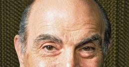 David Suchet smiling, wearing a blue shirt and dark blazer, known for his iconic portrayal of Hercule Poirot.