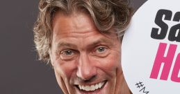 John Bishop smiling and holding a sign promoting kindness, wearing a "say hello" badge for awareness campaign.
