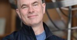 Scott Manley smiling confidently, wearing a black jacket with "Astronomy" logo, standing in a scientific setting.