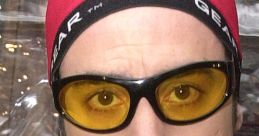 Ali G in a vibrant yellow jacket, yellow sunglasses, and a red beanie, showcasing his iconic hip-hop style and attitude.