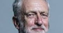 Jeremy Corbyn, prominent British politician, smiling in a formal suit with a blue tie, against a light background.