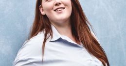 Confident woman with long red hair smiling in a blue striped shirt and jeans, posing against a light blue backdrop.