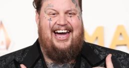 Jelly Roll flashes a joyful smile, showcasing his tattoos and flashy jewelry at a glamorous awards event.