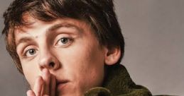 Jacob Bertland poses thoughtfully in an olive green jacket, showcasing unique jewelry and expressive features.