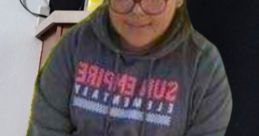 Jimena Friend sitting cross-legged in a cozy gray hoodie, smiling with glasses in a home setting.