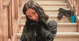 Amber from Scream 5 sits on a staircase in a black outfit, playfully posing with a smile amidst a casual setting.