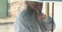 Man with a long beard holding an umbrella and gesturing for silence on a rainy day in Carovigno, Puglia.