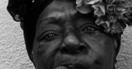 Elderly woman with a cigar and vibrant flowers, showcasing cultural pride and tradition in black and white photography.