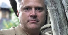 Sean Oliver poses confidently in a stylish beige blazer, surrounded by a natural outdoor setting.