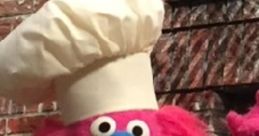Gonger from The Furchester Hotel, a vibrant pink chef puppet with a white hat, cheerfully baking in a cozy kitchen setting.