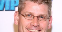 John Anderson smiling at an event, showcasing his signature style with a brown shirt and glasses, exuding warmth and charisma.