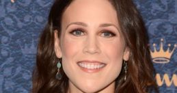 Erin Krakow smiles radiantly at a red carpet event, showcasing her stylish green dress and elegant earrings.