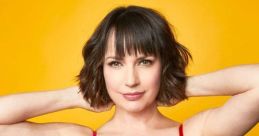 Julie Ann Emery poses confidently in a vibrant pink and red dress against a bright yellow backdrop, showcasing her charisma.