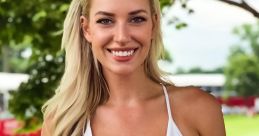 Paige Spiranac smiles brightly, wearing a stylish white top, showcasing her confidence at a golf event in a scenic outdoor setting.