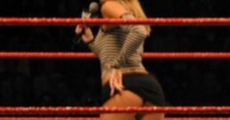 Wrestler in a ring, wearing a striped top and shorts, holding a microphone during a performance with fans in the background.