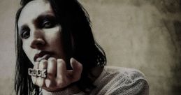 Marilyn Manson poses dramatically in a sheer top, showcasing bold rings and a striking, moody aesthetic.
