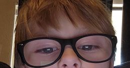 Child with glasses and a small cut on the lip, sitting on a couch, focused and serious expression.