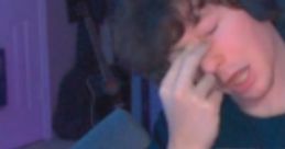 Person with dark, messy hair in a gaming setup, showing an exaggerated expression, with text below saying, "Cute emo slut pony.