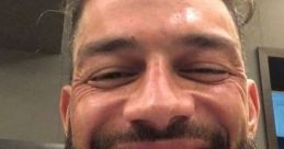 Roman Reigns flashing a big smile, showcasing his signature beard, radiating charm and charisma in a casual setting.