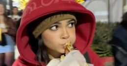 Maddison Jackson enjoying street food in a cozy red hoodie, surrounded by festive lights and a lively crowd.