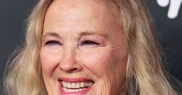Catherine O'Hara smiles warmly at a red carpet event, showcasing her signature style and vibrant personality.