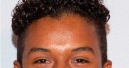 Jaafar J. Jackson smiles brightly at an event, showcasing his curly hairstyle and stylish attire, reflecting youthful charisma.