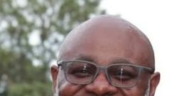 Smiling man in red shirt with glasses, showcasing a friendly demeanor outdoors, representing warmth and approachability.