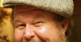 Smiling man in a gray cap, showcasing a warm personality and a friendly demeanor, reminiscent of Ned Beatty's charm.