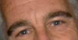 Close-up of a man with silver hair and blue eyes, exhibiting a subtle smile, with a neutral background.
