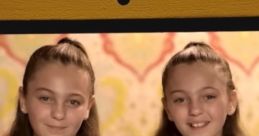 Kelly and Carla twins smiling together, both wearing matching light blue shirts, showcasing their playful personalities.