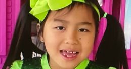 Jannie smiles brightly in a sparkling green outfit, featuring a large green bow, against a colorful backdrop.