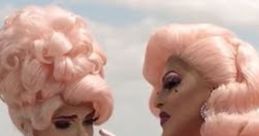 Two glamorous drag performers in pink outfits share a tender moment outdoors, embodying the vibrant spirit of AAMI Advert.