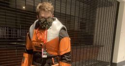 Person wearing a vibrant orange Hev Suit costume, complete with a mask, posing in a convention center setting.