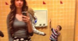 Teen girl taking a selfie in a restroom mirror, with a child playfully gesturing in the background.