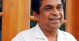 Brahmanandam smiles warmly while holding a camera, showcasing his signature charm and personality.