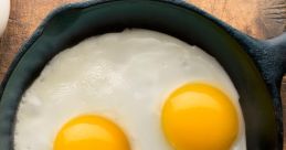 Two sunny-side-up eggs in a cast-iron skillet on a wooden surface, showcasing their vibrant yellow yolks.