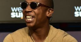 Ja Rule smiles during an event, showcasing his style with sunglasses and accessories, reflecting his vibrant personality.