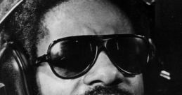 Stevie Wonder passionately singing into a microphone, showcasing his iconic sunglasses and soulful expression.