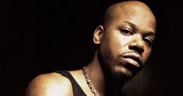 Too $hort poses confidently in a dark setting, showcasing his distinctive style and strong presence in hip-hop culture.
