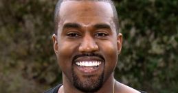 Kanye West smiling while wearing a black shirt and gold necklace, surrounded by greenery in a sunny outdoor setting.
