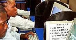 Individuals using computers in an office setting, with signs warning against scams and phishing emails.