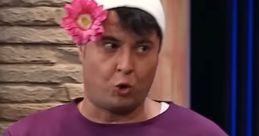 Comedic character in purple outfit, wearing a white hat and flower, showcasing humorous expressions from Güldür Güldür Show.