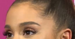 Ariana Grande smiling with a natural makeup look, showcasing her signature high ponytail against a vibrant pink backdrop.